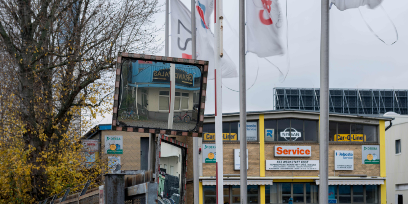 Fahnenmasten und Spiegel vor einem Industriegebäude mit Werbeschildern