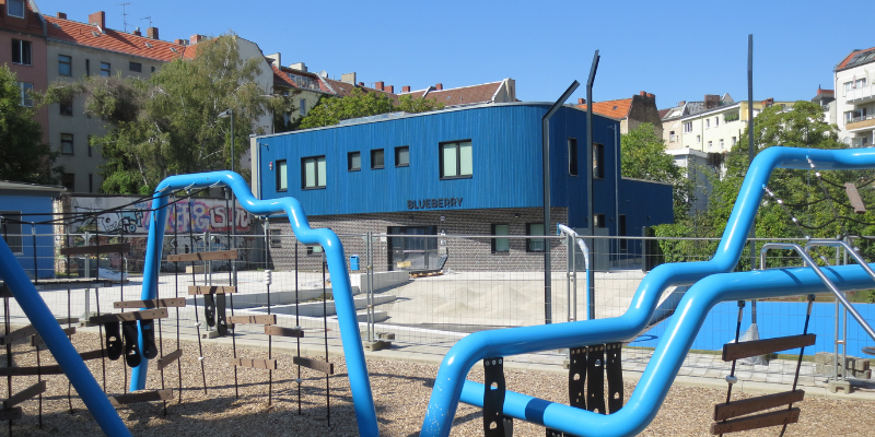 Spielplatz mit blauen Elementen und im Hintergrund ein blaues Haus