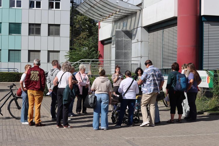 Eine Gruppe von Menschen steht vor einem Gebäude, eine Person erzählt etwas