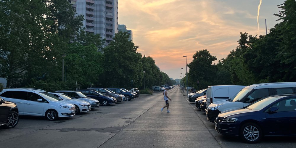 Blick in eine Straße mit beidseitig parkenden Autos und querender Person.