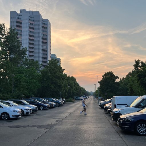 Blick in eine Straße mit beidseitig parkenden Autos und querender Person.