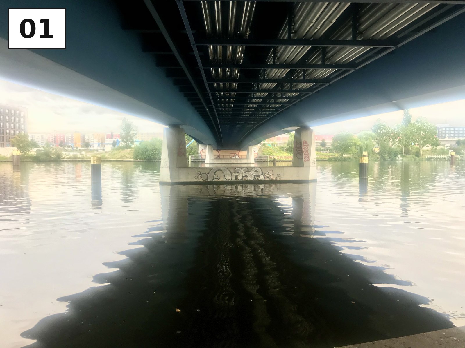 Blick knapp über dem Wasser unter eine Spreebrücke, die Stahlträger spiegeln sich