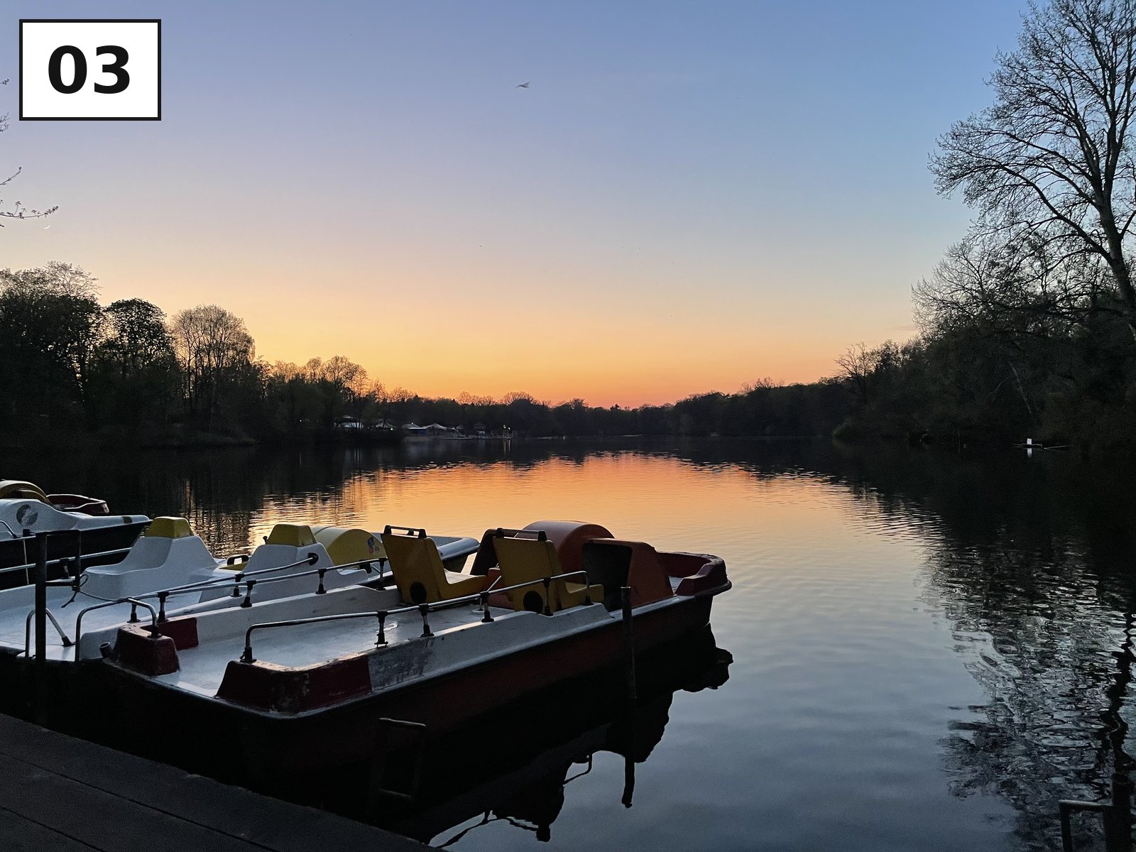 Tretboote am Ufer, dahinter geht die Sonne über dem Wasser unter