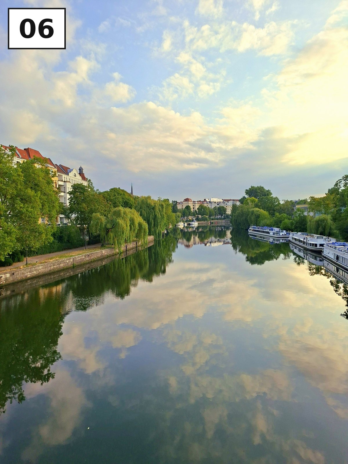 Wolkenhimmel spiegelt sich im glatten Kanal, Bäume säumen das Ufer