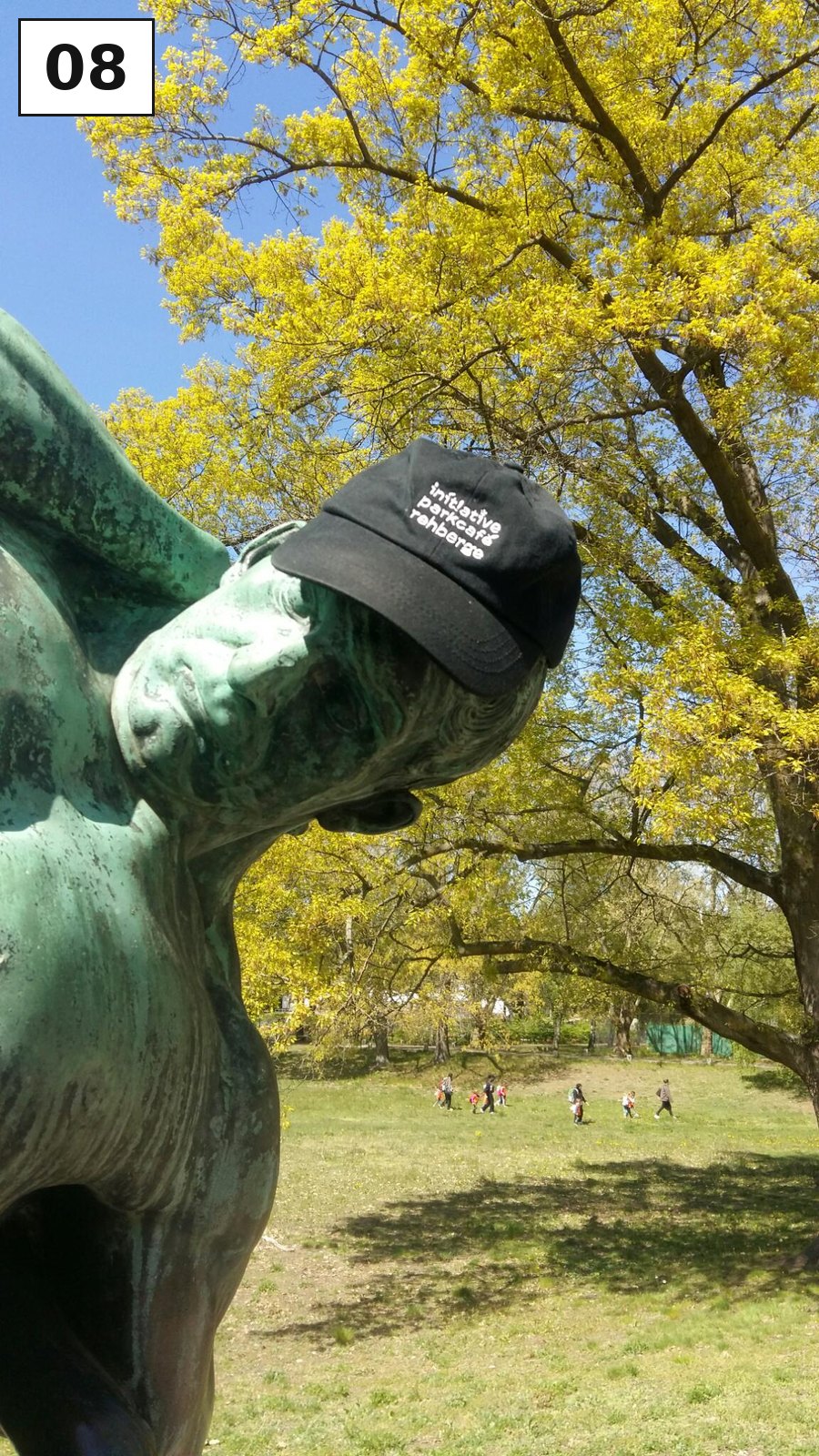 Bronzeskulptur mit aufgesetzter Kappe unter einem Baum auf einer Wiese