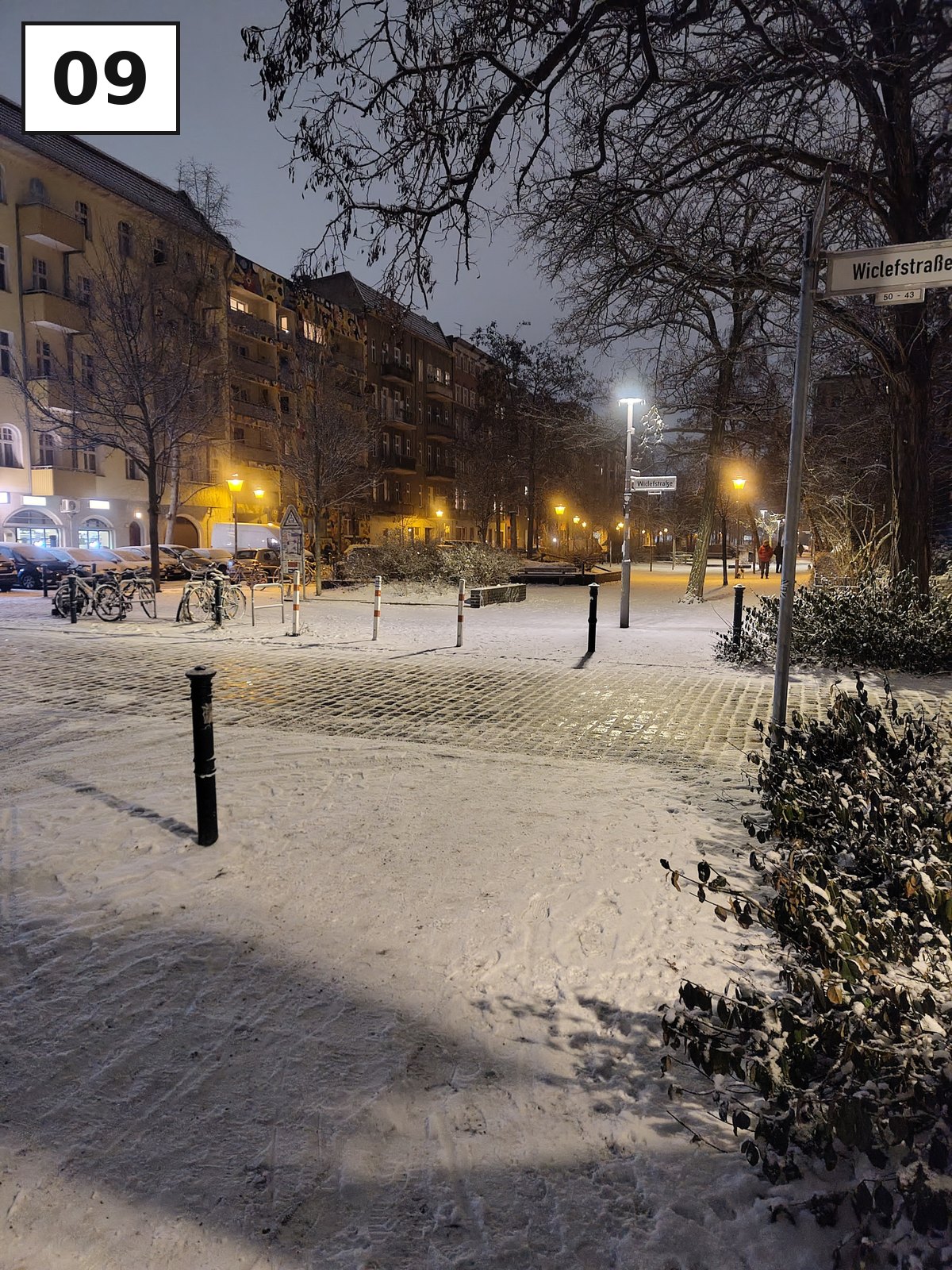 Verschneiter Gehweg mit Laternen und Altbauten am Abend
