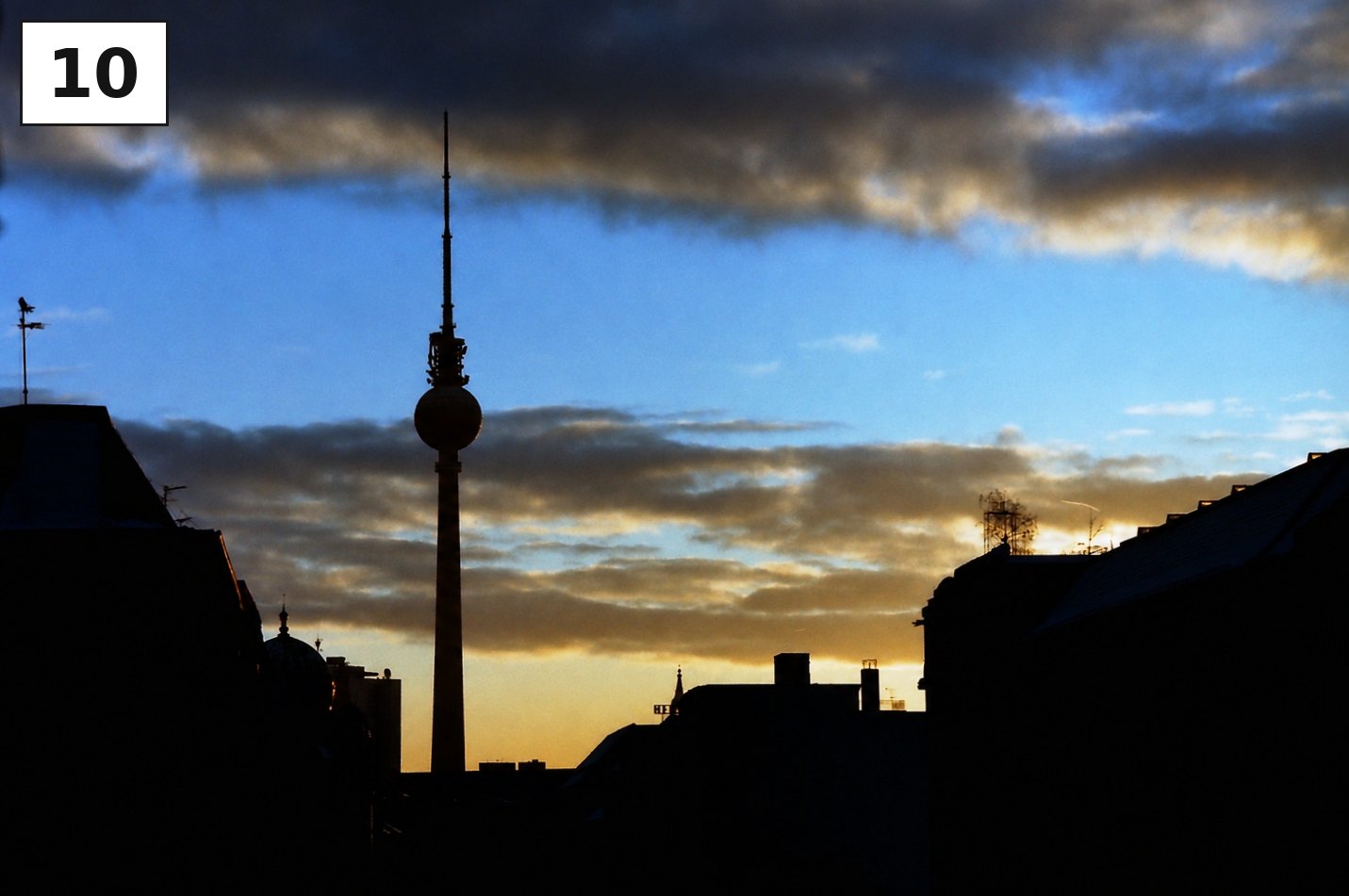 Silhouette des Fernsehturms zwischen dunklen Häuserzeilen bei Sonnenuntergang
