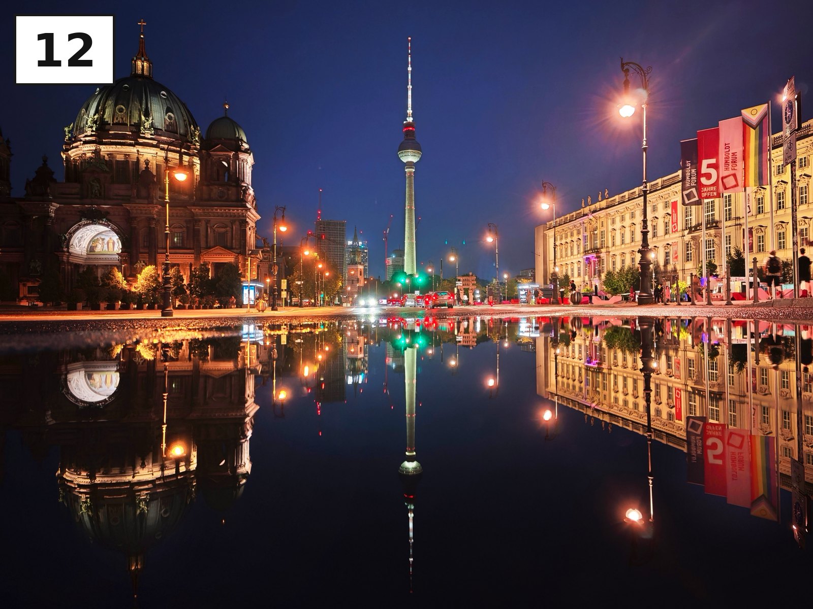 Berliner Dom und Fernsehturm spiegeln sich nachts in einer nassen Fläche