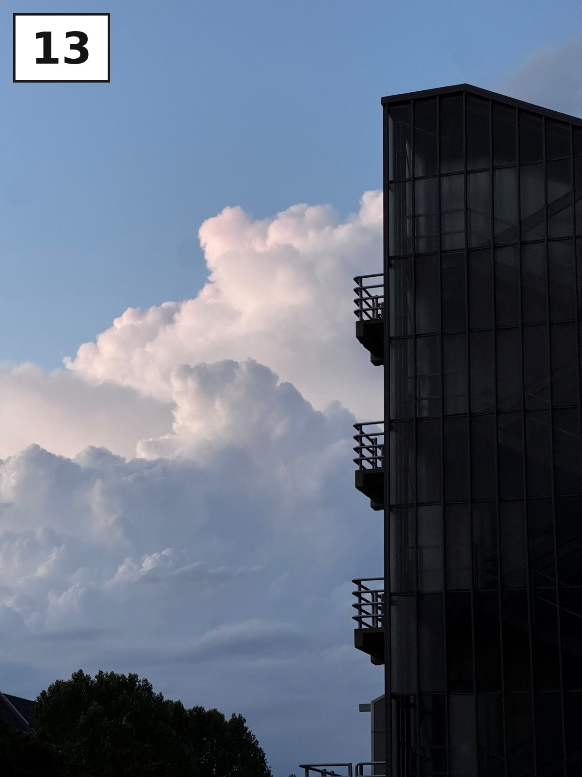 Dunkle Glasfassade, daneben eine hohe weiße Wolke am blauen Himmel