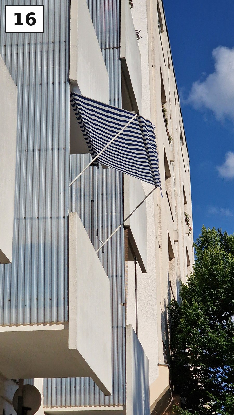 Weiße Hausfassade mit einer Fahne am Balkon vor blauem Himmel