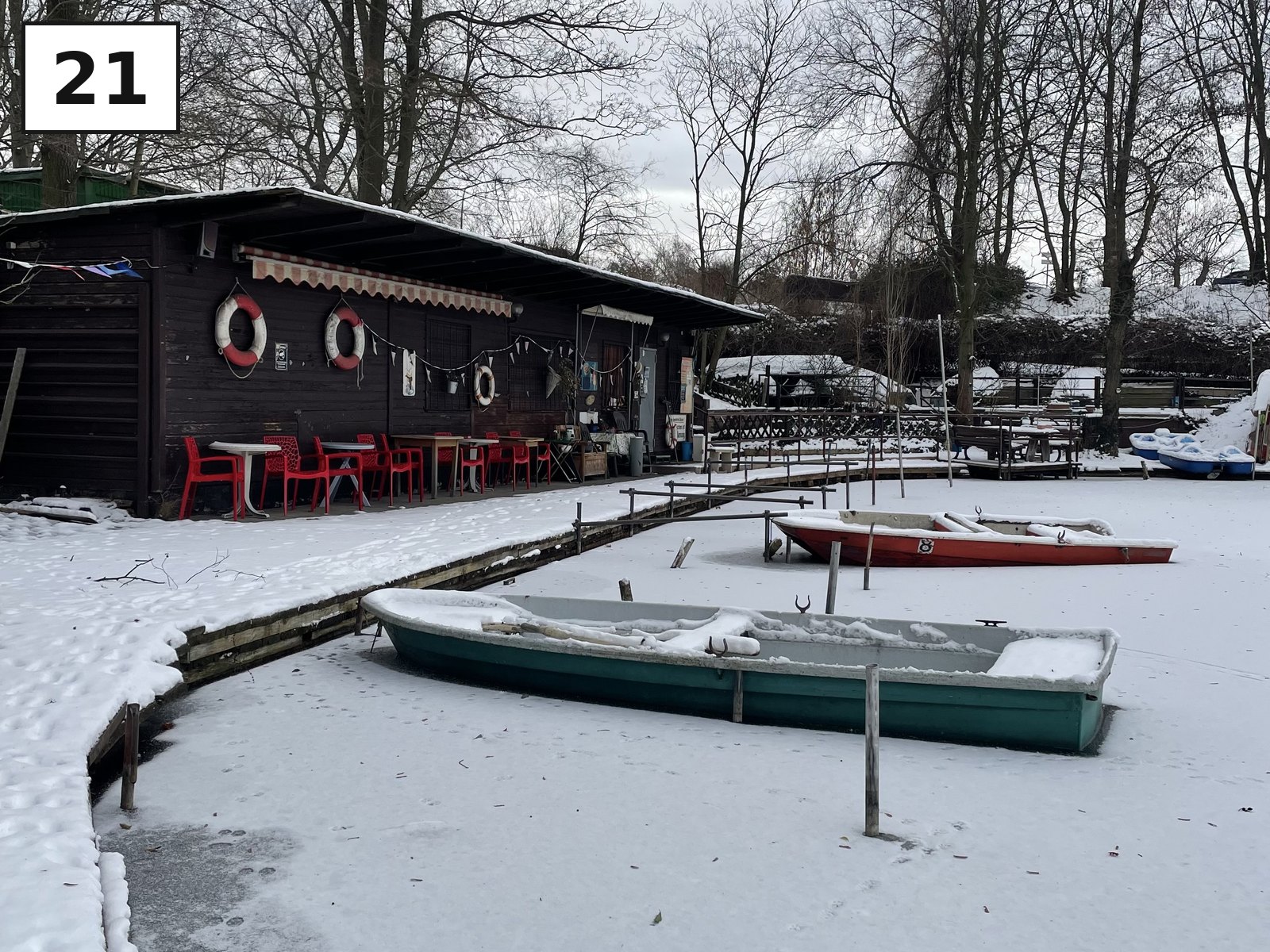 Ruderboote im Schnee vor einem Bootshaus am Wasser